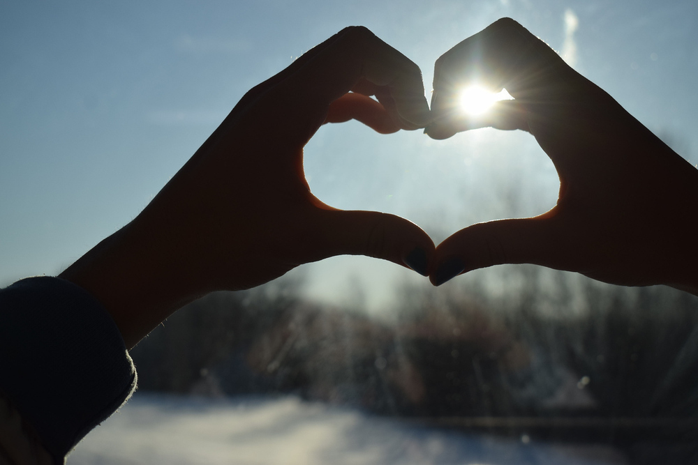 Hände bilden ein Herz durch das die Sonne scheint. 